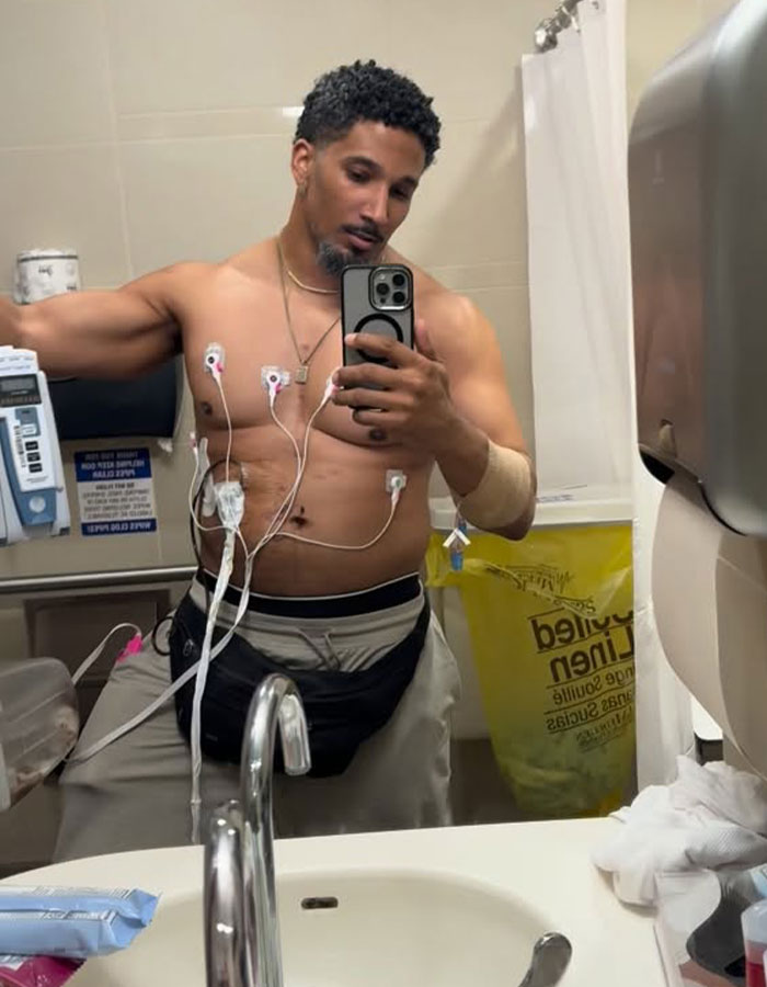 A man needing a transplant, taking a mirror selfie in a bathroom, connected to medical sensors and equipment.