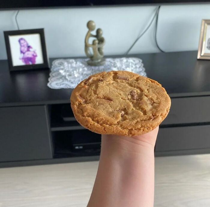 A hand holding a giant cookie, needing a second look to understand the optical illusion in this photo.