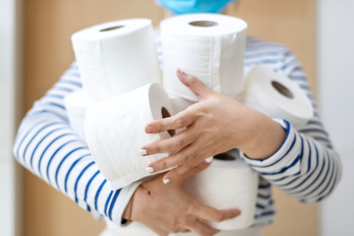 A person in a mask holding a large stack of toilet paper, relating to guests ignoring house etiquette.
