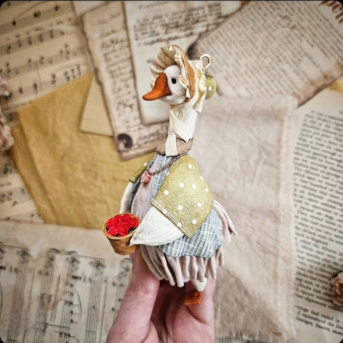 A handmade cotton wool creation of a goose holding a basket of flowers, against a vintage paper background.