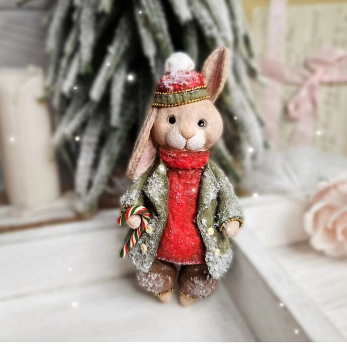A handmade cotton wool creation of a rabbit in a winter coat, hat, and holding a candy cane.