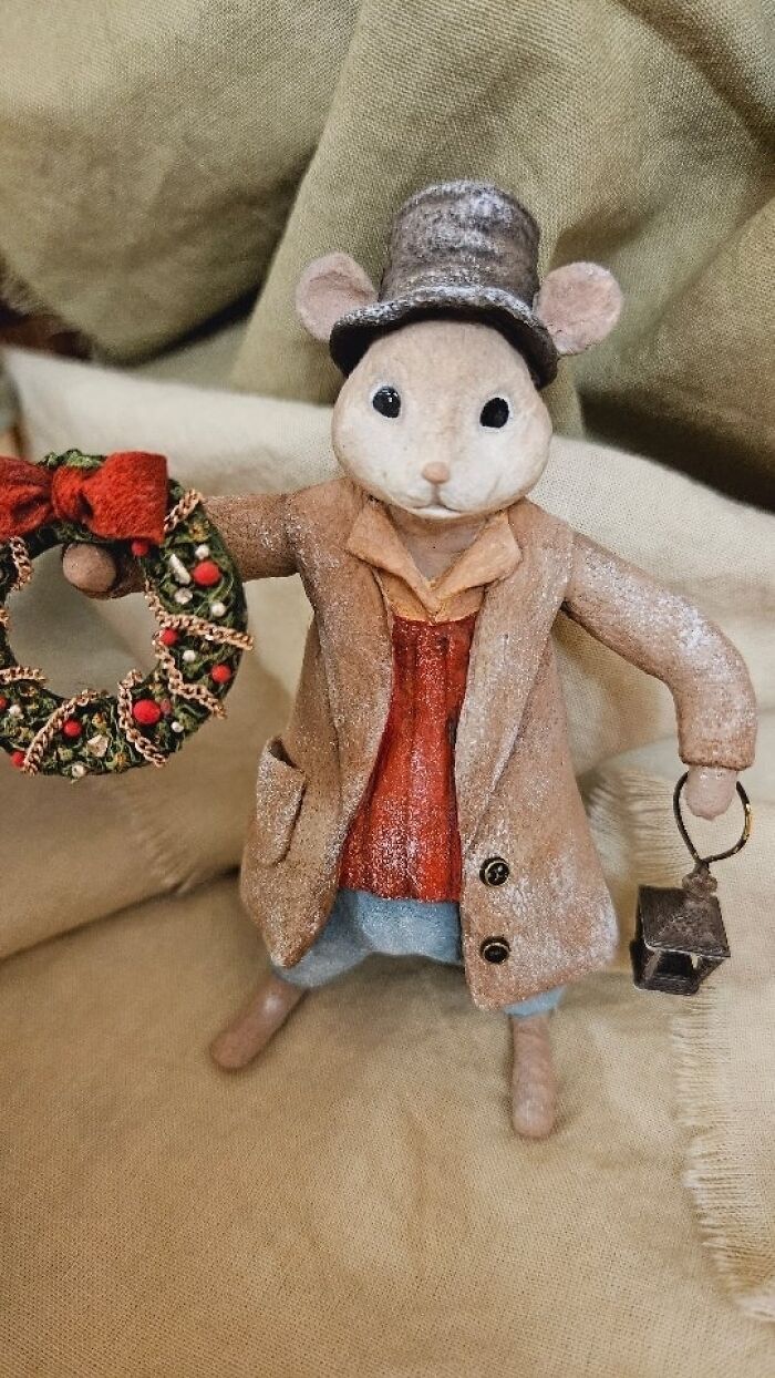 A handmade cotton wool creation of a mouse in a brown coat, top hat, holding a wreath and lantern.