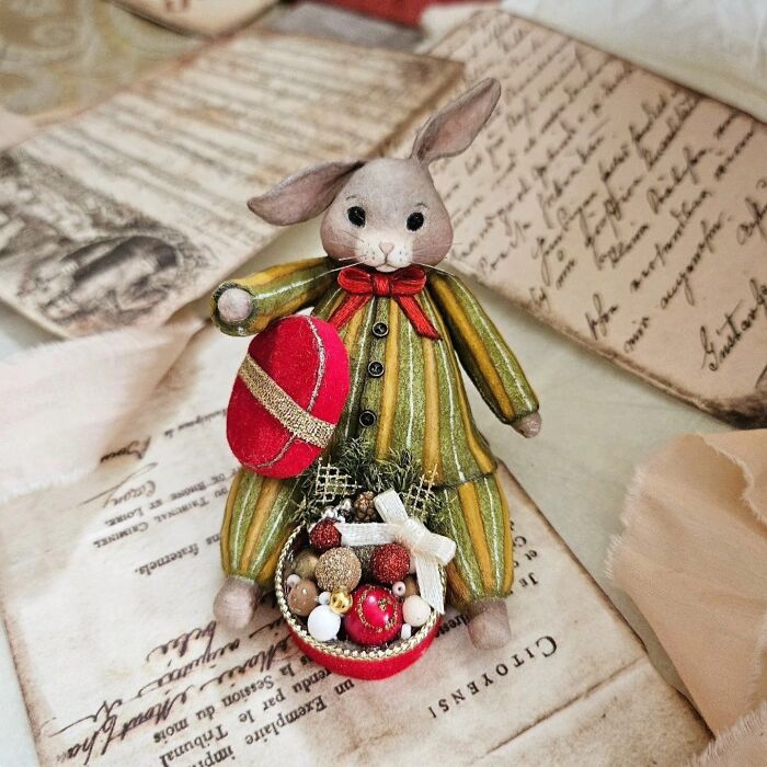 A handmade cotton wool creation of a rabbit in striped pajamas holding a red egg and a basket of ornaments.