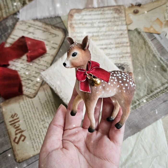 Handmade cotton wool creation of a deer with a red bow and bell, held in a hand against vintage papers.