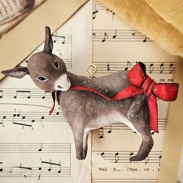 Handmade cotton wool creation of a donkey with a red bow, standing on a vintage music sheet.