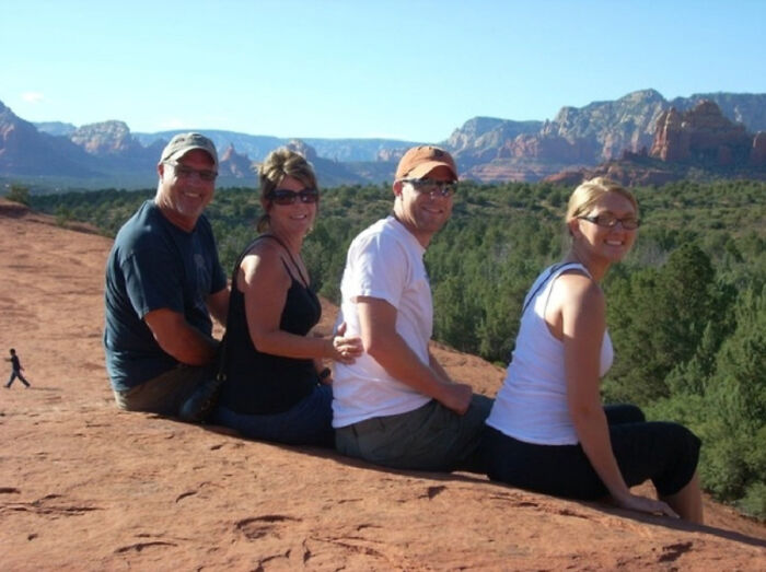 Real photo of four people sitting in a line on a rock formation, creating an optical illusion that makes the brain question if it was edited.