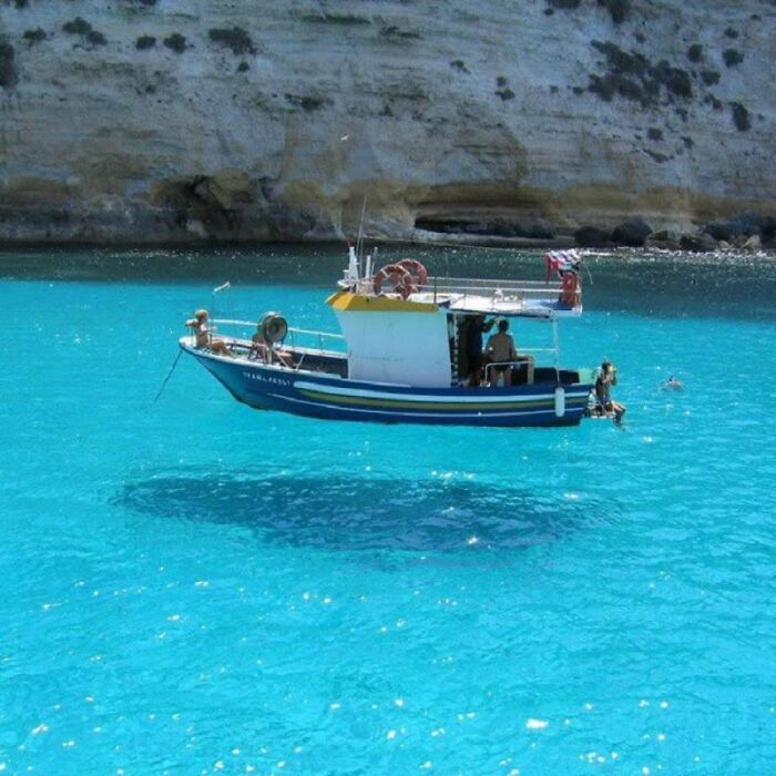 Real photo of a boat appearing to float in incredibly clear, blue water, making the brain question if it was edited.