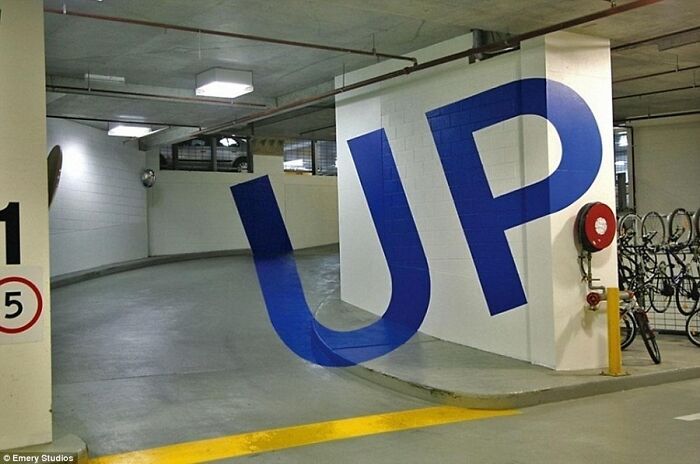 A parking garage with the word UP painted to create a 3D illusion, a real photo that makes your brain question if it was edited.