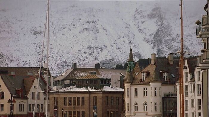 Historic buildings with pointed roofs in front of snow-covered mountains, a real photo that makes your brain question if it was edited.