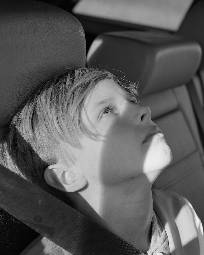 Best black and white photographs: a young boy with light hair in a car seat looking upwards, sun on his face.