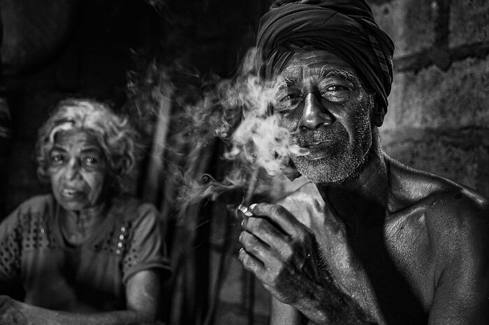 A man with a turban smokes, with smoke swirling around him. A compelling black and white photograph.