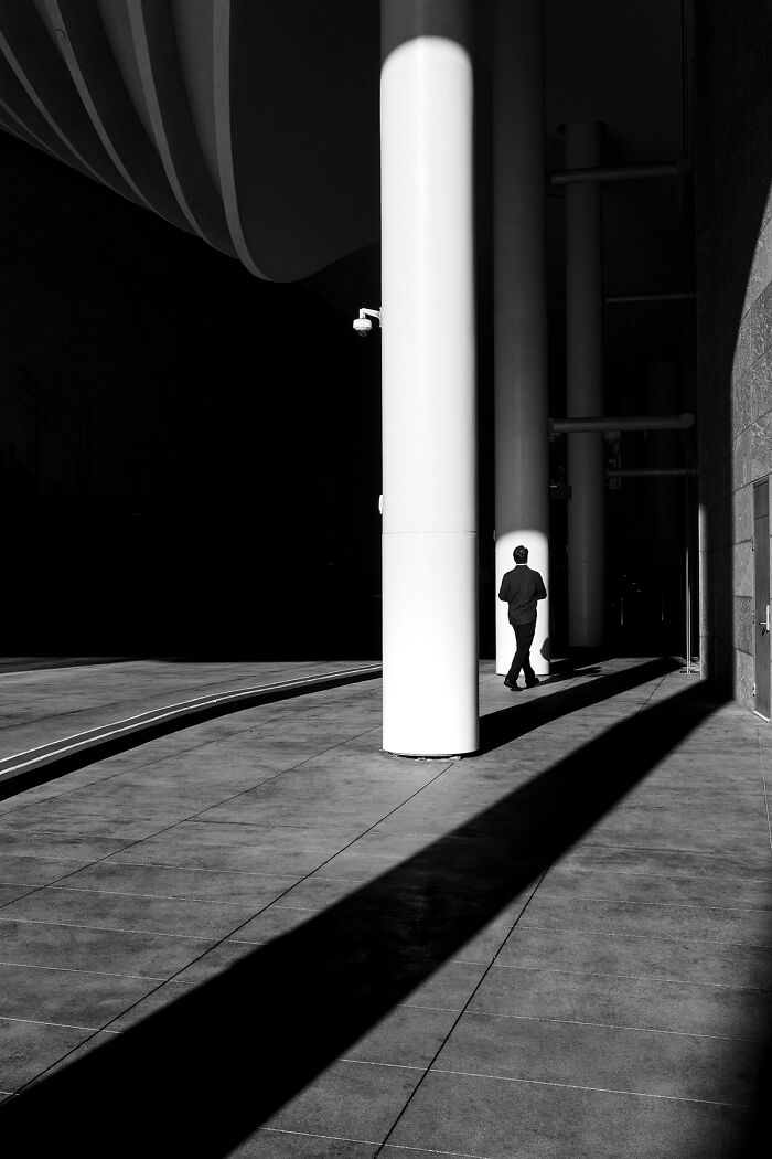 Best black and white photographs of a person walking in shadow, past large white pillars.