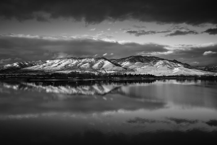 Best black and white photographs showcasing snow-capped mountains reflecting in a lake under a cloudy sky.