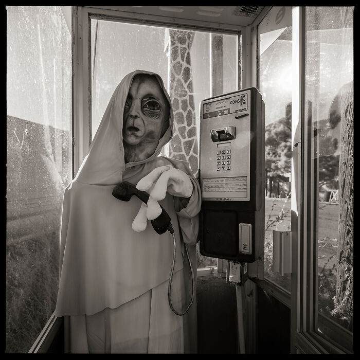 Best black and white photographs: an alien figure in a cloak holding a phone receiver in a phone booth.