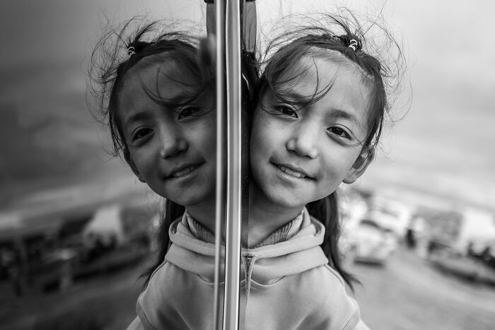 Reflective black and white portrait of a smiling girl, her reflection perfectly aligned.