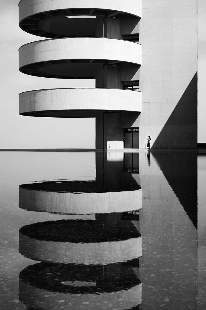 Best black and white photographs: a person by a modern building with circular balconies reflecting in water.