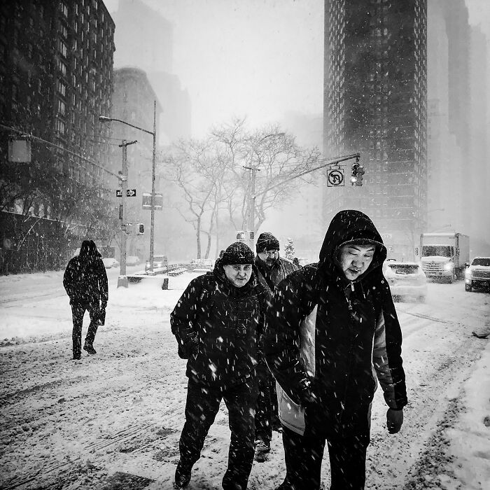 Pedestrians navigate a snowy city street, an impactful black and white photograph.