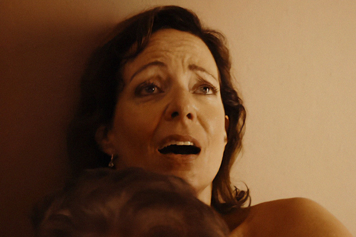 A woman in an intimate scene, her expression revealing behind-the-scenes chaos.