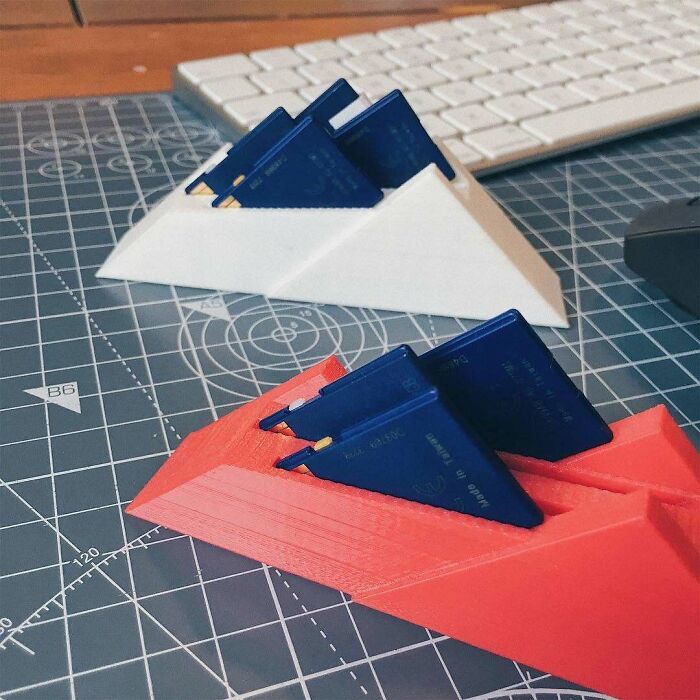 A close-up of two 3D printing creations, one white and one red, holding small blue items on a grey cutting mat. Amazing 3D printing creations.