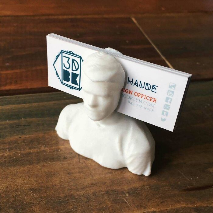 A white 3D printing creation of a bust holding business cards on a wooden surface. Amazing 3D printing creations.