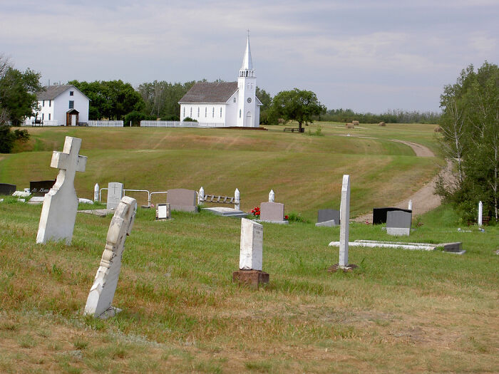 A serene graveyard with various tombstones in the foreground, and a white church on a hill, symbolizing unsolved mysteries.
