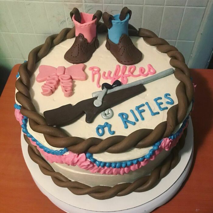 A Gender Reveal cake featuring pink boots, a rifle, and the text 'Ruffles or Rifles'. Parents are being judged.