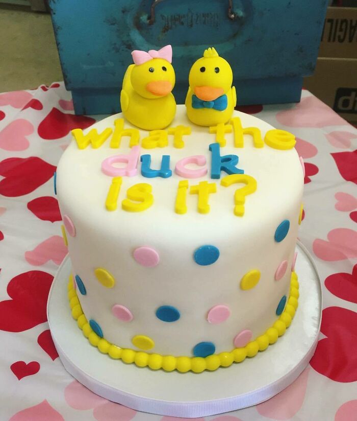 A gender reveal cake decorated with yellow and blue polka dots, featuring duck figurines and the phrase what the duck is it?