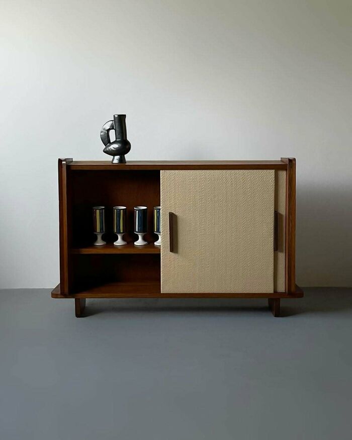 A brilliant design choice for a sleek, modern wooden cabinet with a sliding woven door and decorative vase.