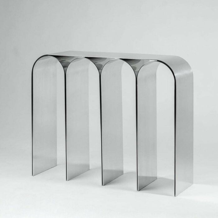 A modern, clear console table with brilliant design choices, featuring arched, reflective legs.