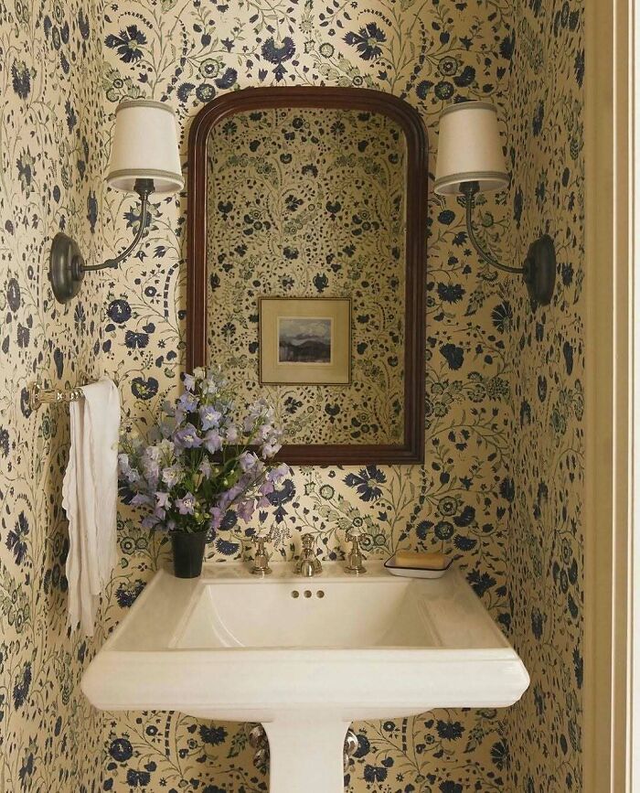 A brilliant design choice for a small bathroom with floral wallpaper, a pedestal sink, and an elegant mirror.