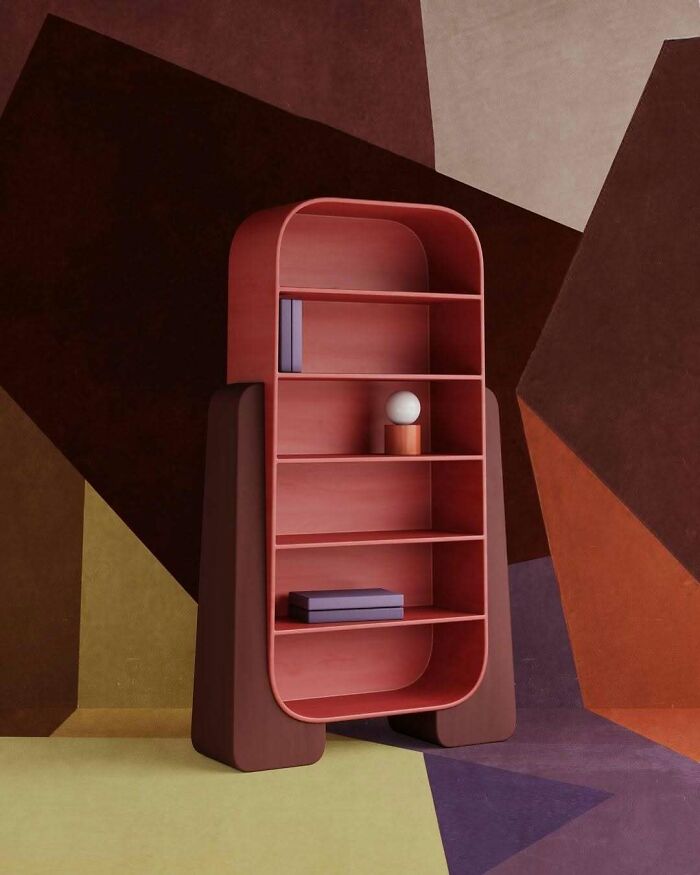 A unique, rounded red bookshelf with various shelves, standing on two wide brown legs, displaying brilliant design choices.