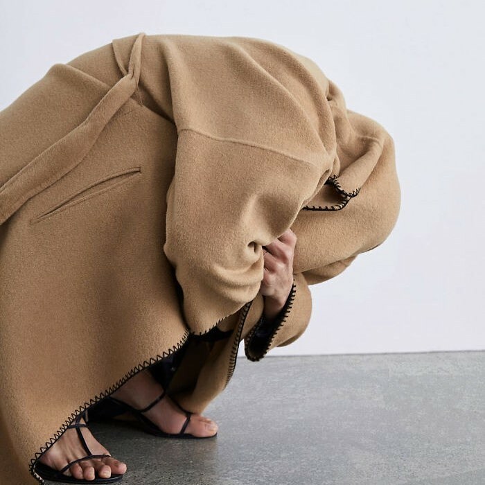 A person hunched over, completely hidden in an oversized coat, as seen in bizarre content on the Zara website.
