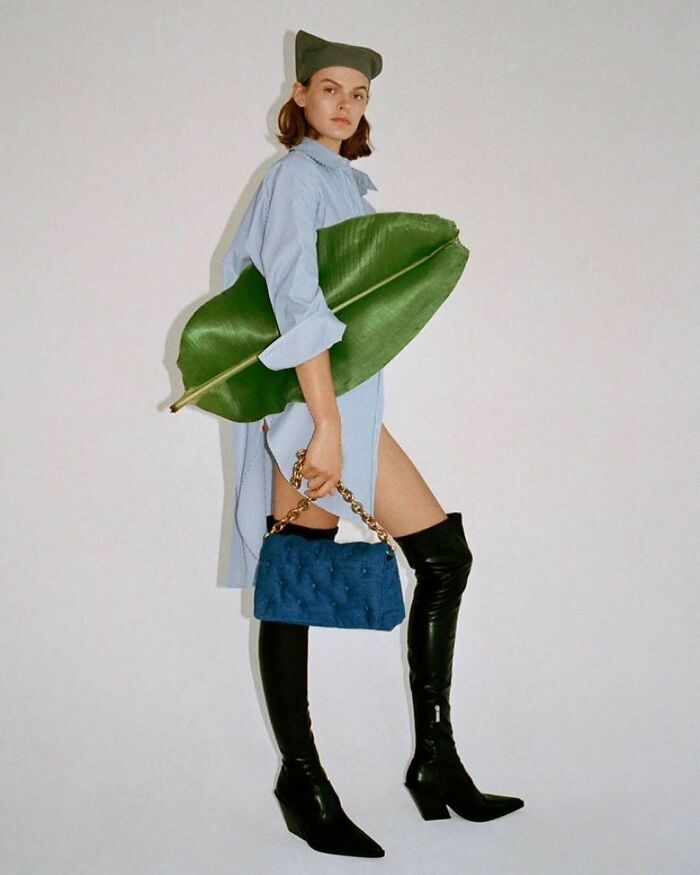 A model holding a large banana leaf, wearing a blue shirt and black boots in bizarre Zara website content.