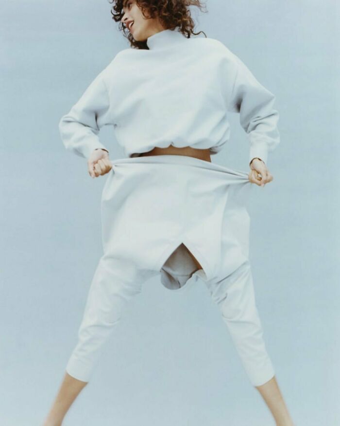 A woman in bizarre Zara content, wearing loose white clothing, appears to be mid-jump against a light blue background.