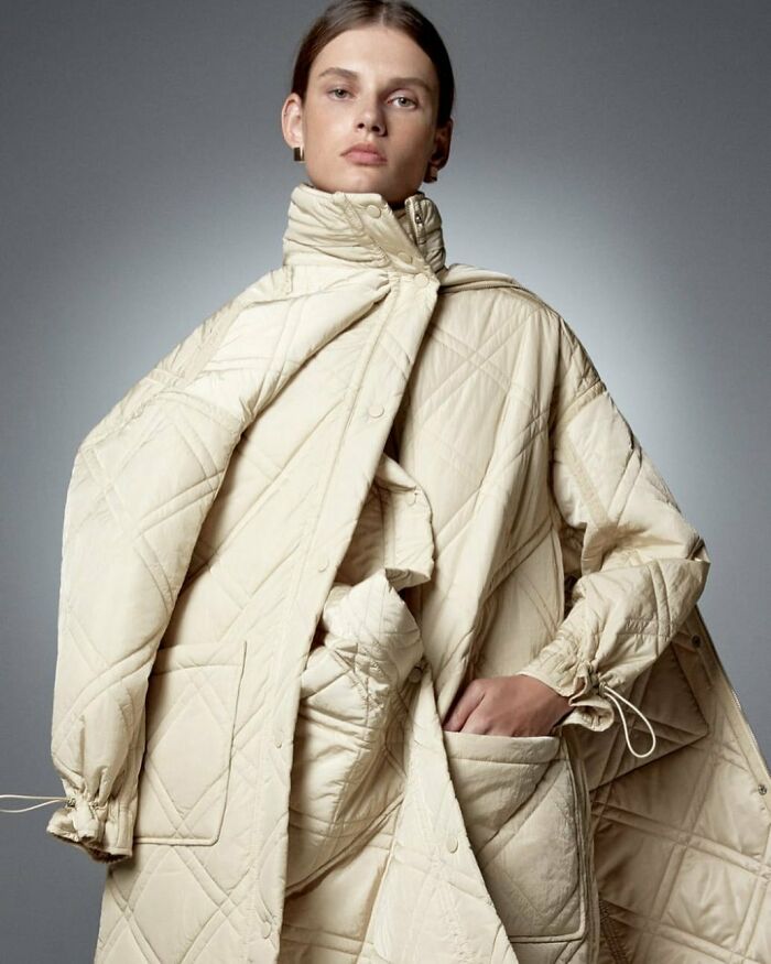 A woman wearing an oversized quilted beige coat, highlighting bizarre content found on the Zara website.