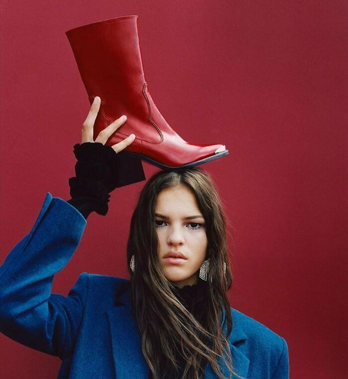 A woman holding a red boot on her head, showcasing bizarre content on the Zara website.