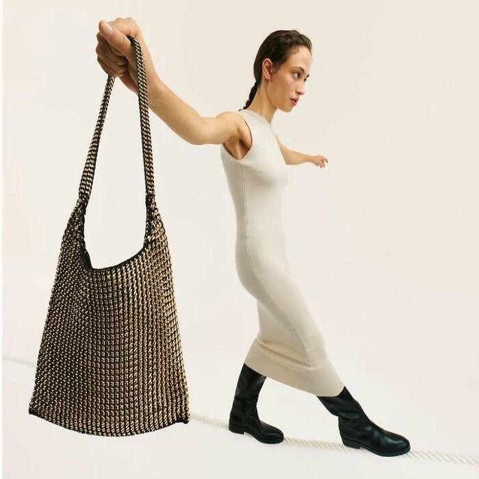 A woman in a long dress and boots balances on a rope while holding a large bag, part of Zara's bizarre content.