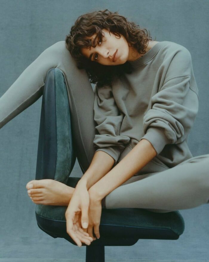 A woman in bizarre Zara content with curly hair, sitting on a chair, wearing a grey sweatshirt and matching pants.