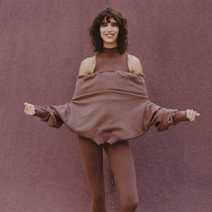 A smiling woman in a brown, oversized, off-the-shoulder sweatshirt and leggings, representing bizarre Zara content.