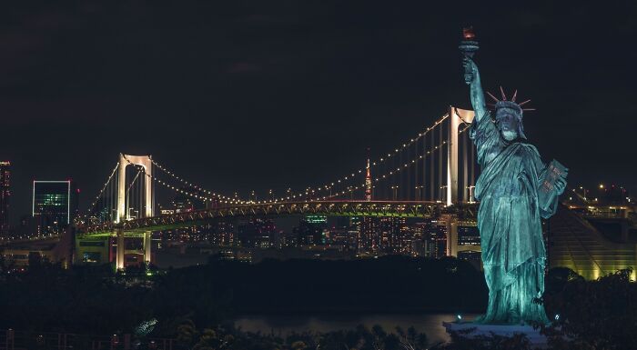 Nighttime view of a statue resembling the Statue of Liberty with a brightly lit suspension bridge in the background, a challenging landmark to decode. Nighttime view of a statue resembling the Statue of Liberty with a brightly lit suspension bridge in the background, a challenging landmark to decode.