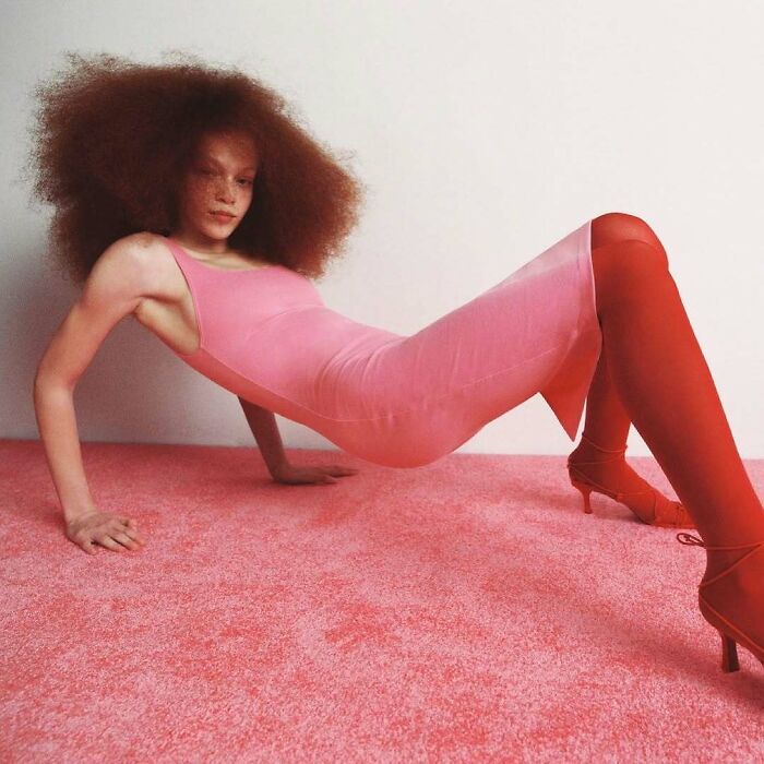 Bizarre content on Zara website: a model in a pink dress and red tights poses oddly on a pink carpet.