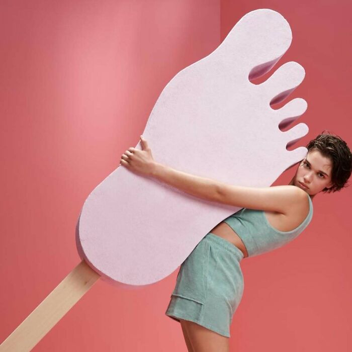 A woman embracing a giant foot popsicle stick, showcasing bizarre content on the Zara website.