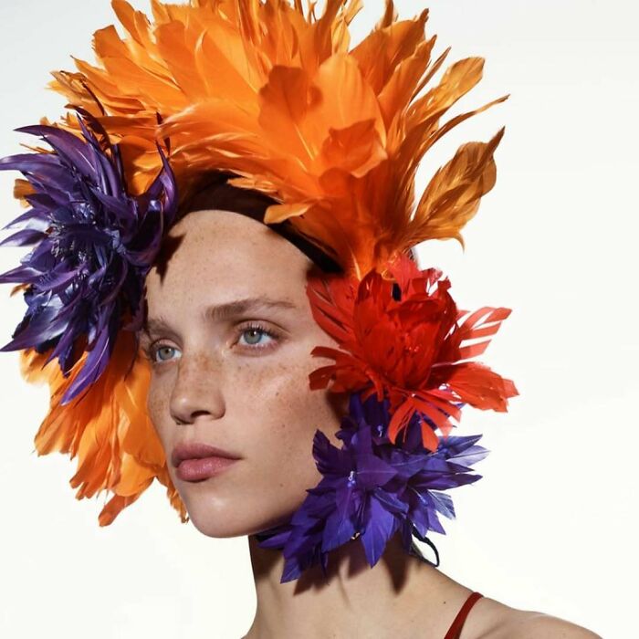 A woman with an elaborate feather headpiece in orange, red, and purple, bizarre content on the Zara website.