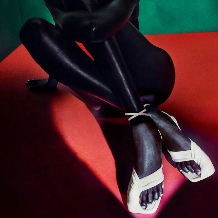 Dark-skinned legs and feet wearing white sandals on a red surface, showcasing bizarre content on Zara website.