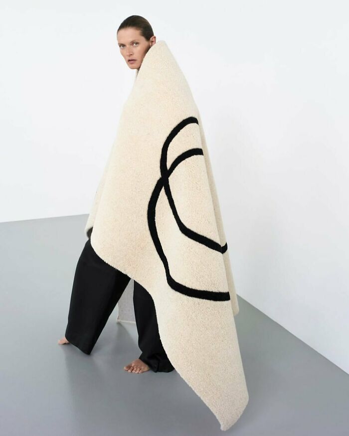 A model draped in a large, bizarre content Zara blanket with black circular designs, looking over her shoulder.
