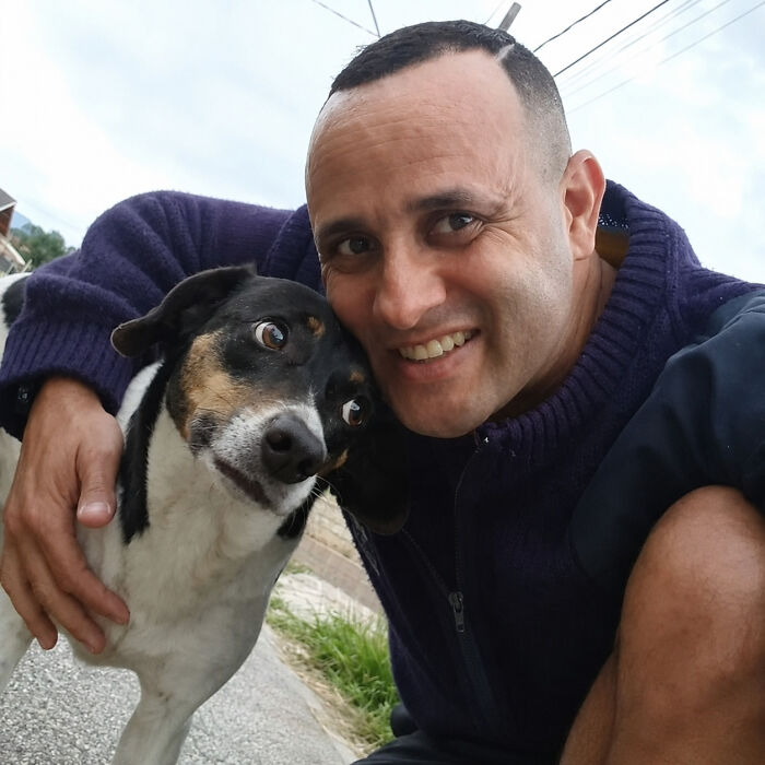 A kind mailman embraces a small dog, stopping to befriend dogs during his deliveries, with a wide smile.