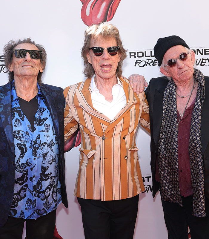 Three country singers pose on a red carpet, attending a music event with other country singer fans.