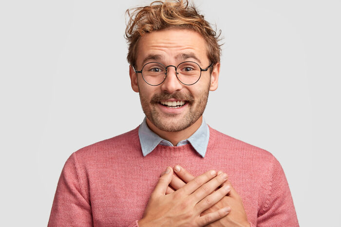 A man with messy hair and glasses smiling with hands on his chest, showing sincerity in amazing comebacks.
