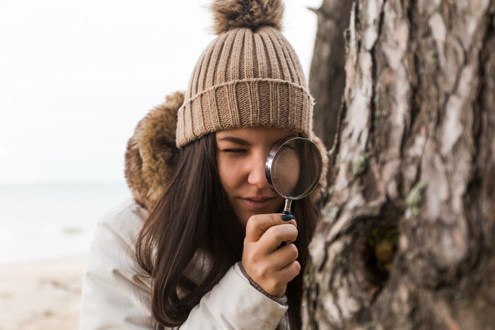 A woman with a magnifying glass by a tree, metaphorically searching for amazing comebacks.