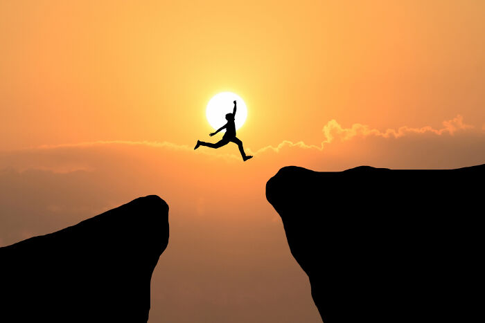 Silhouette of a person jumping across a cliff at sunset, symbolizing amazing comebacks.